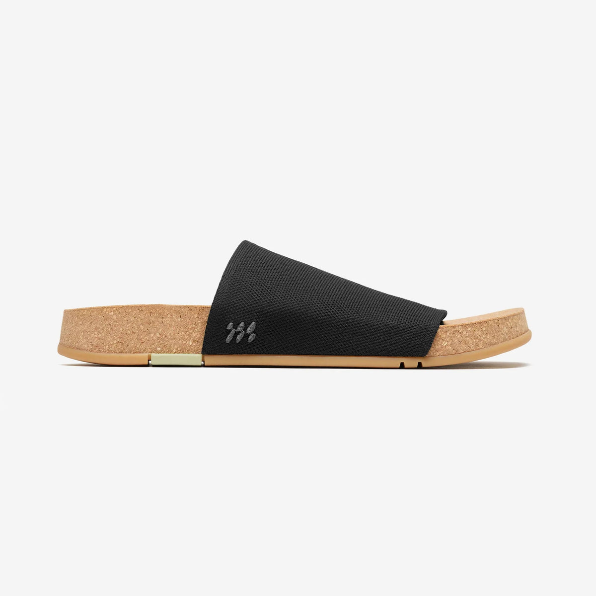 Black slide sandal viewed from the side, featuring a woven strap and natural cork footbed with a natural rubber sole.