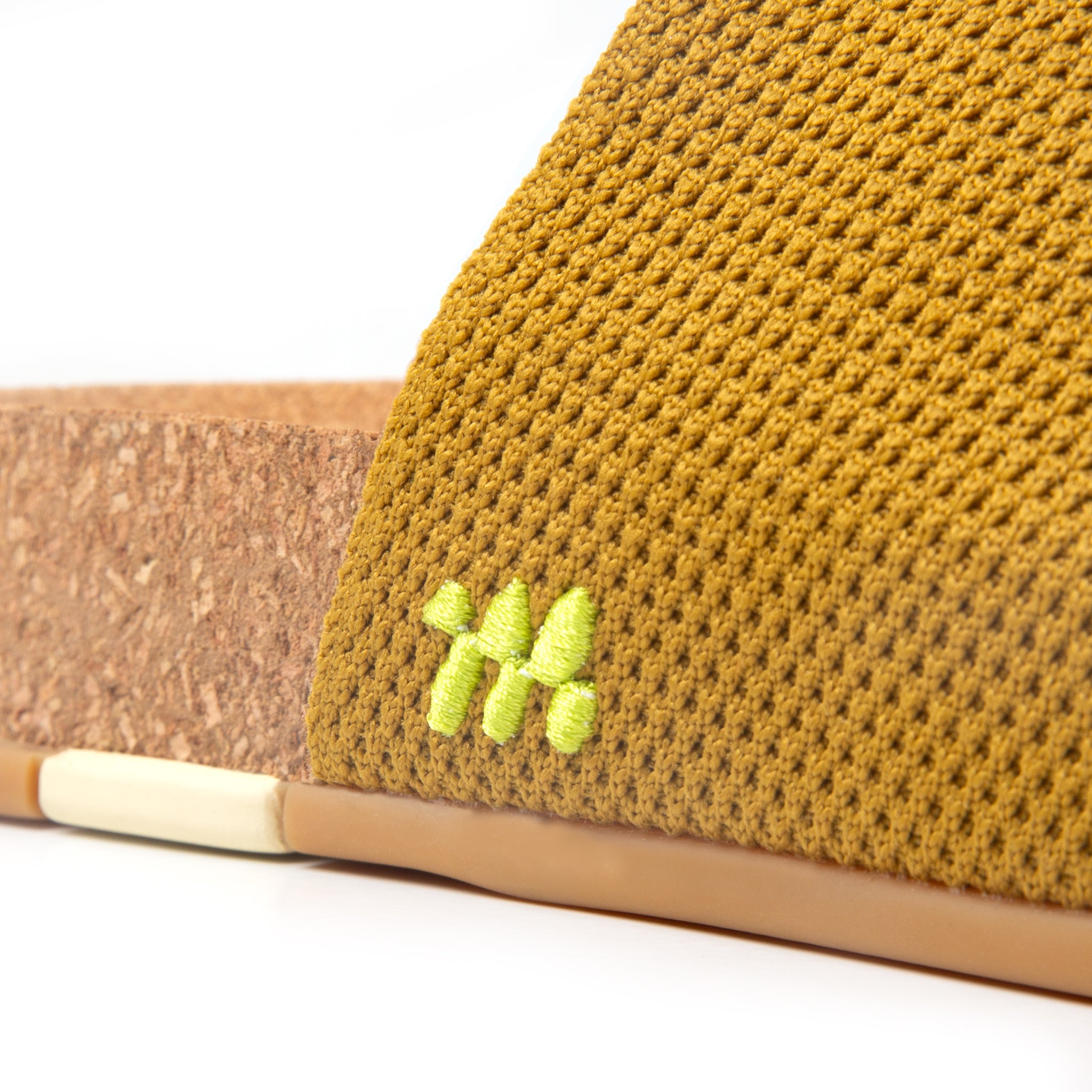 Close-up of a mustard yellow woven sandal with a brown insole on a white background