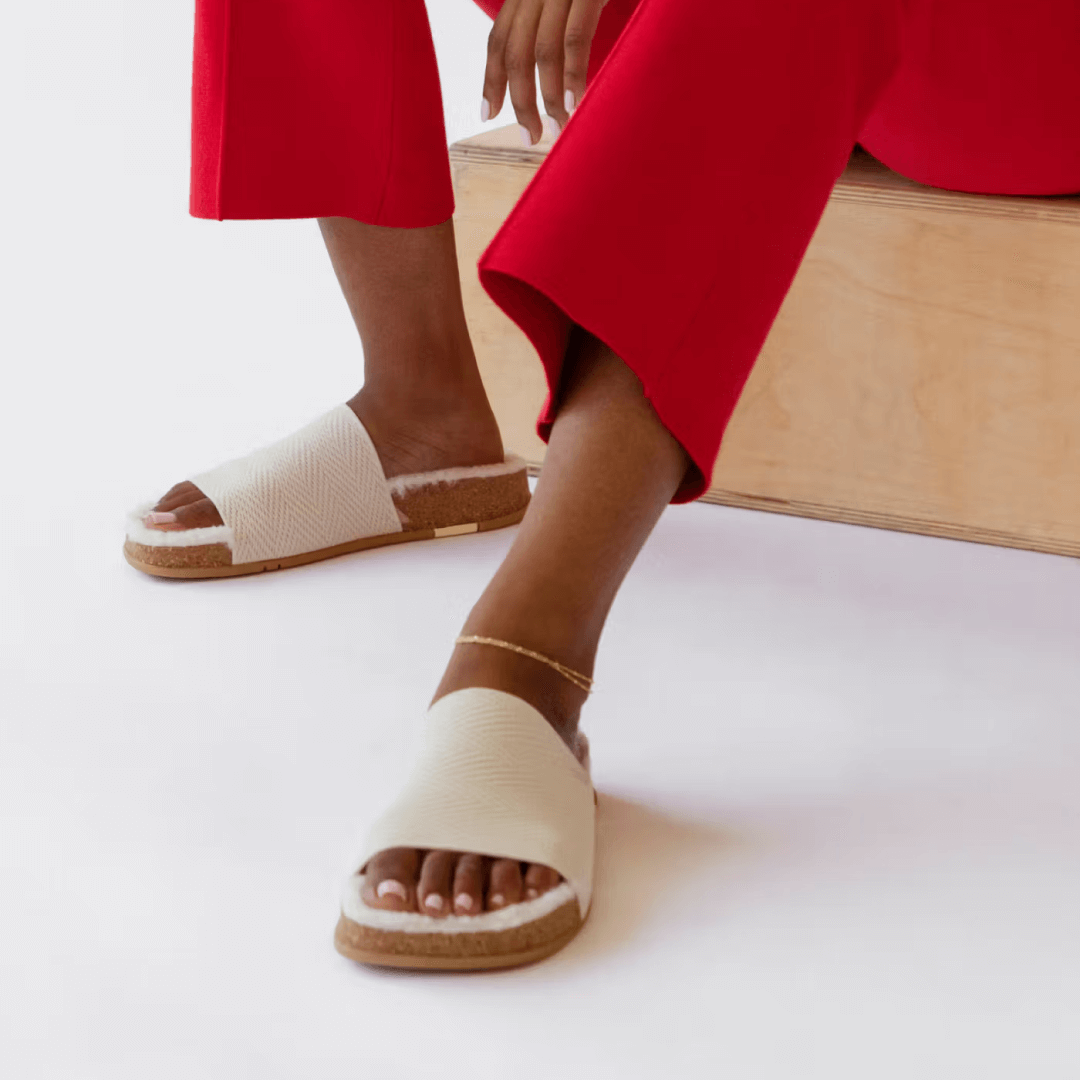 Woman wearing a pair of creme Shaw Cozy Slides. Featuring Vegan eco-shearling™️ recycled cotton custom blend