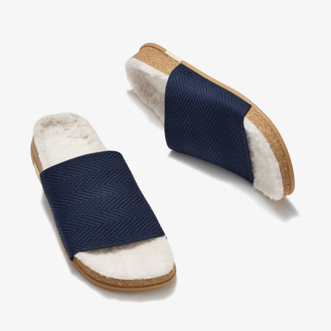 A pair of MESSAGE Navy Midnight Cozy Shaw Slides with cream vegan shearling and cork footbeds.
