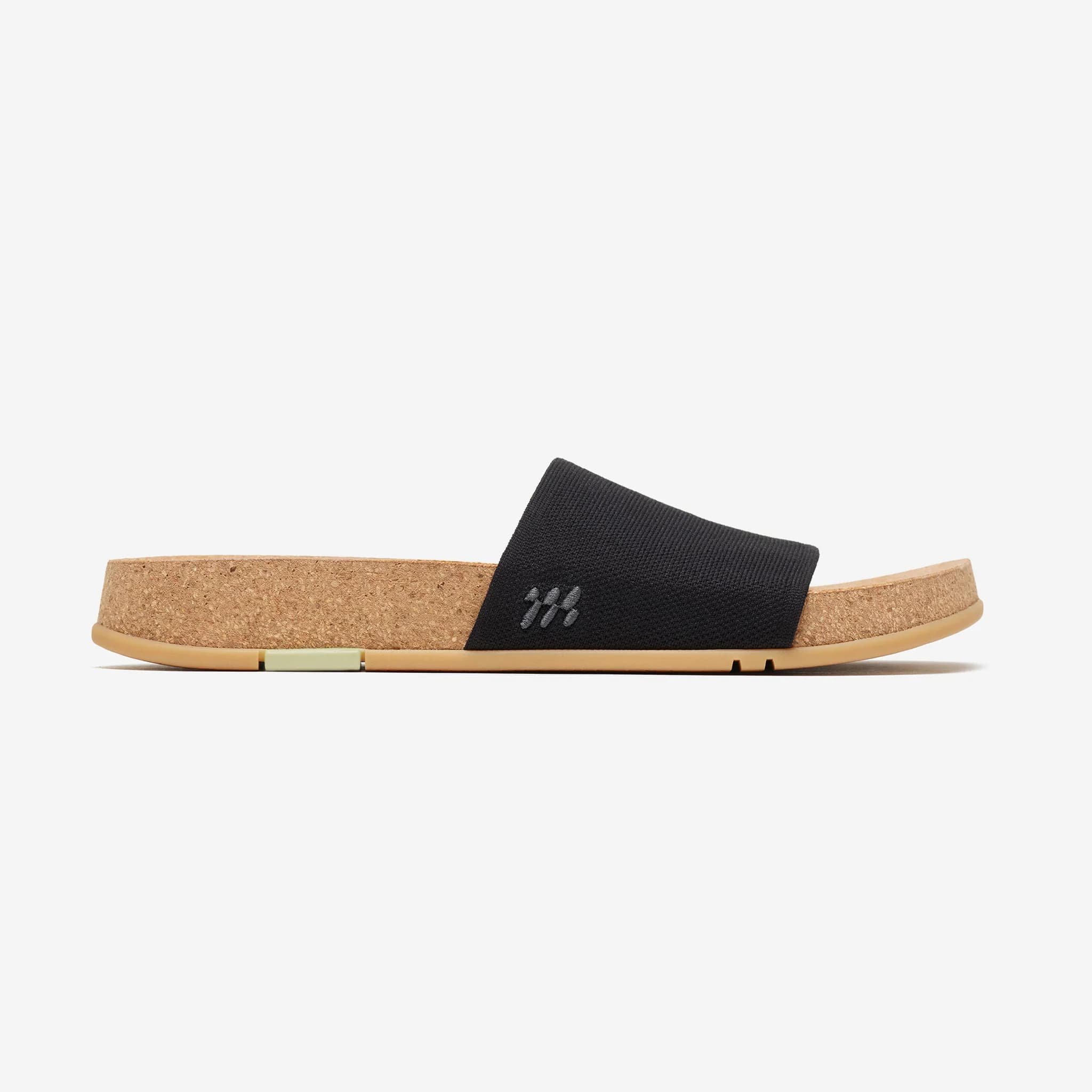 Black slide sandal with cork footbed and gum outsole shown in profile, highlighting the knit upper and logo detail.