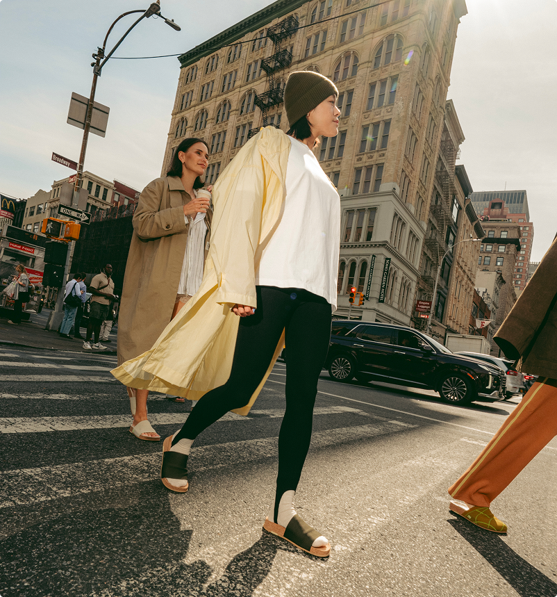 Two women crossing a city street with tall buildings in the background