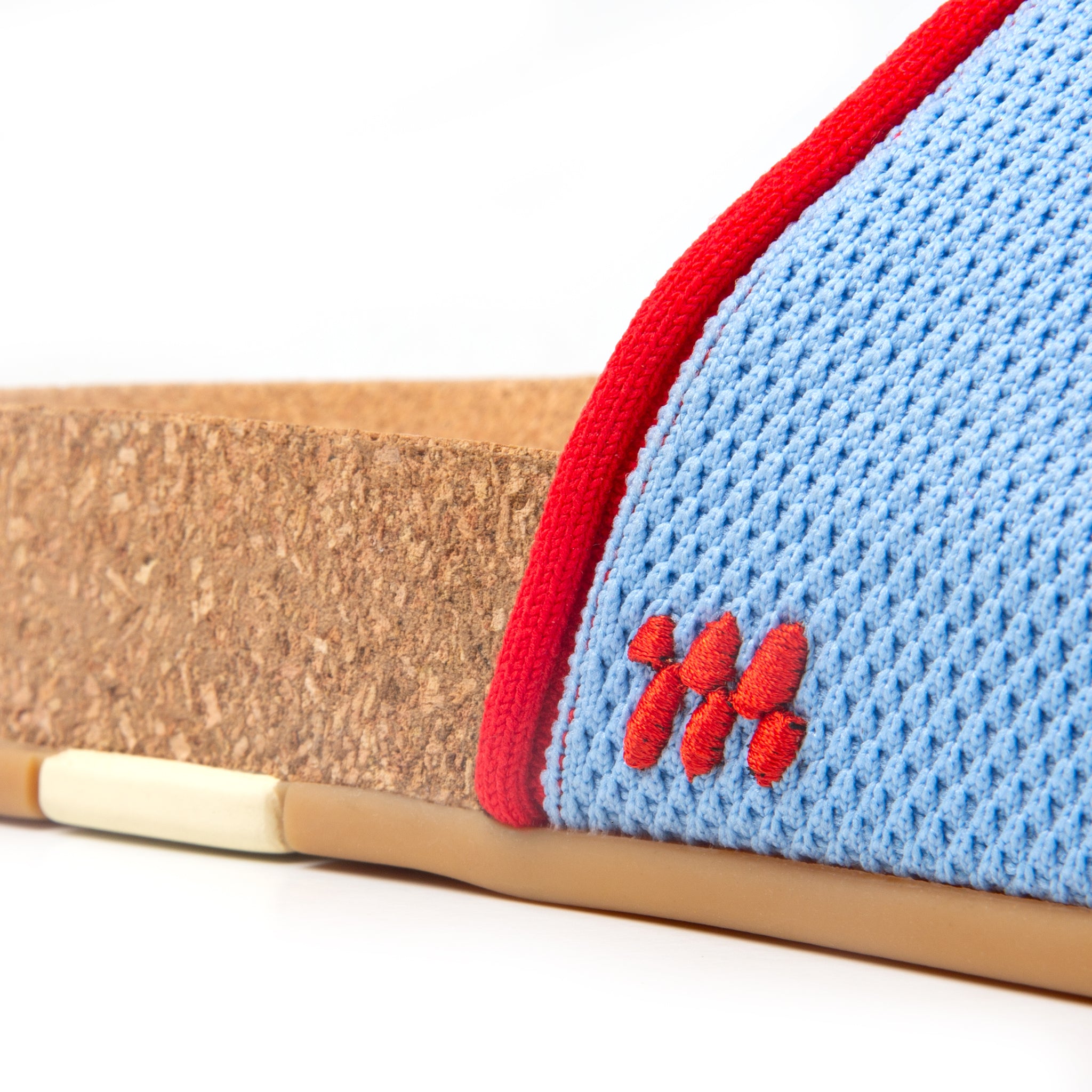 Close-up of a sandal with blue mesh, red trim, and brown sole on a white background